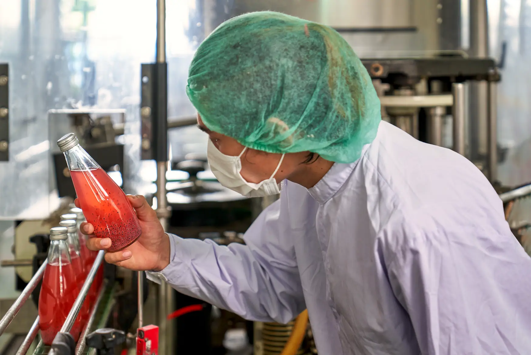 worker inspects liquid in a bottle on a production line